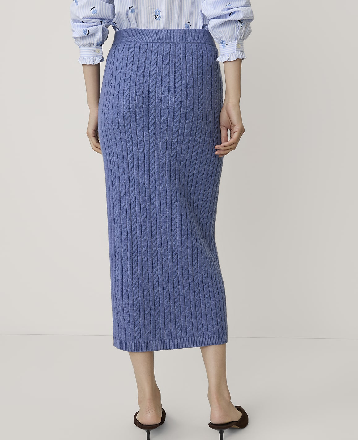A person wears a blue cable-knit midi skirt and a striped blouse against a plain, light-colored background.