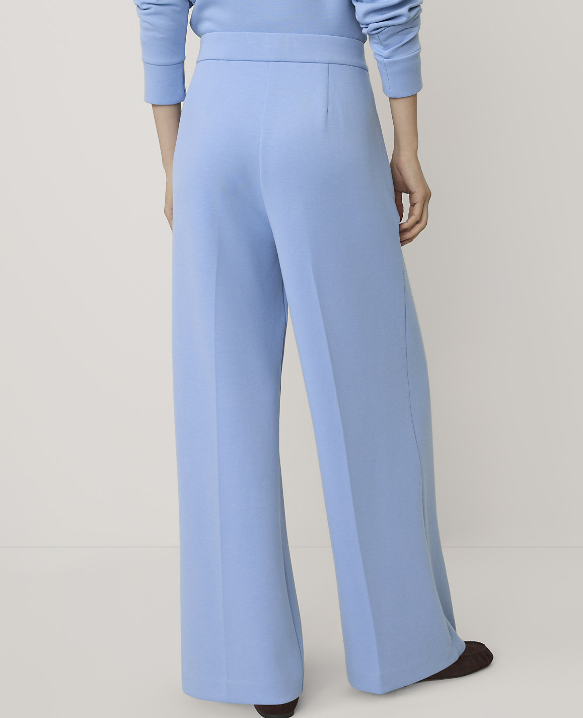 A person wearing light blue wide-leg trousers and a matching top stands against a plain, neutral background.