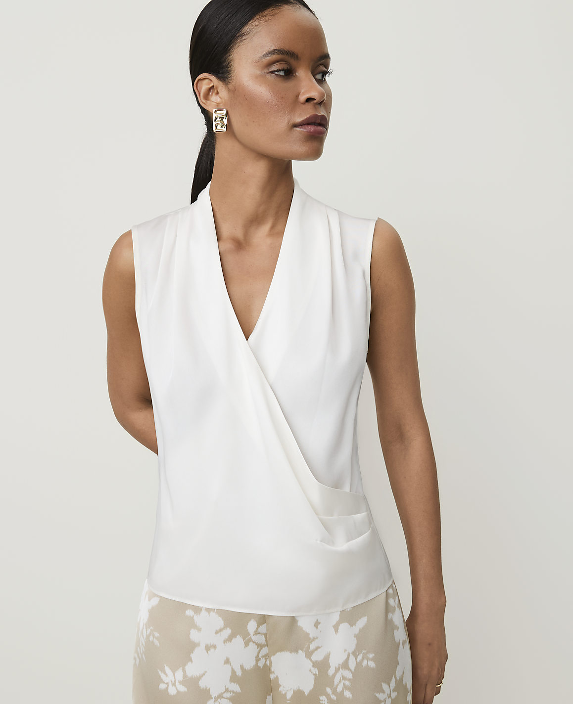 A woman in a white wrap top and floral skirt stands against a plain background.