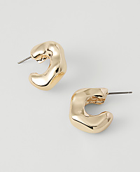 Two gold, abstract-shaped hoop earrings with post backs rest on a plain, light gray background. carousel Product Image 1