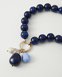 A close-up of a necklace with large blue beads and dangling charms rests on a plain white background. carousel Product Image 2
