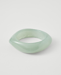 A translucent, pale green, abstractly shaped bangle rests on a plain white background. carousel Product Image 1