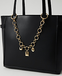 A black tote bag with a gold chain and charms hangs in the foreground against a plain white background. carousel Product Image 1