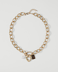 A gold chain necklace with a heart pendant and two charms rests on a plain white background. carousel Product Image 1