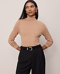 A woman in a tan turtleneck and black pants stands against a plain beige background. carousel Product Image 1