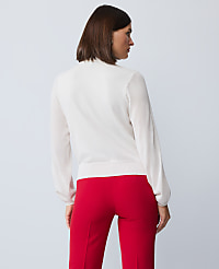 A woman in a white sweater and red pants stands against a plain, light blue background. carousel Product Image 2