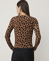 A woman in a leopard print top and black pants stands against a plain, light-colored background. carousel Product Image 2