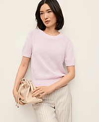 A woman in a light pink sweater and pinstripe pants holds a beige drawstring bag against a plain white background. carousel Product Image 1