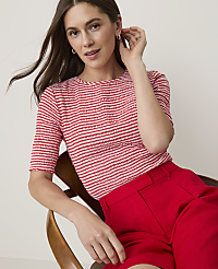 A woman in a red and white striped top and red pants sits on a wooden chair against a plain background. carousel Product Image 3