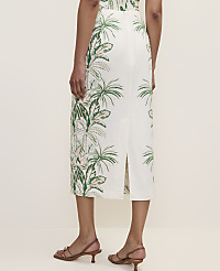 A person stands in the foreground wearing a white skirt with a green tropical leaf pattern, while the background is a plain, light-colored wall. carousel Product Image 3