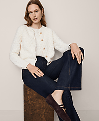 A woman in a cream textured cardigan and dark wide-leg jeans sits on a wooden stool against a plain, light background. carousel Product Image 1
