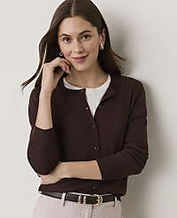 A woman in a brown cardigan and white shirt smiles gently against a plain, light-colored background. carousel Product Image 1