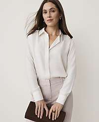 A woman in a cream blouse and plaid pants holds a dark clutch in front of a plain background. carousel Product Image 1
