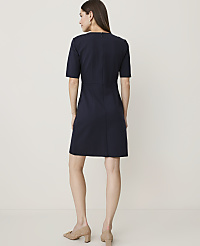A woman in a navy blue dress stands against a plain, light-colored background. carousel Product Image 2