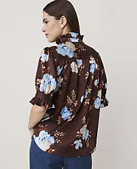A woman in a brown floral blouse with ruffled sleeves and collar stands against a plain, light-colored background. carousel Product Image 2
