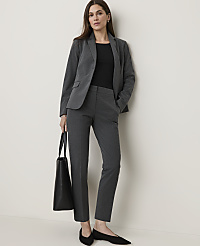 A woman in a grey suit stands against a plain white wall, holding a black tote bag. carousel Product Image 1
