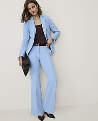 A woman in a light blue suit and brown top stands against a plain white background, holding a dark clutch. carousel Product Image 1
