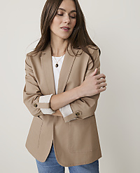 A woman in a tan blazer and jeans stands against a plain, light background. carousel Product Image 1