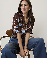 A woman in a floral blouse and jeans sits on a wooden chair against a plain background. carousel Product Image 3