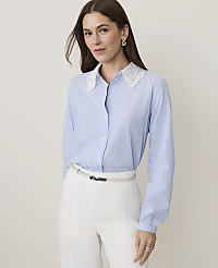 A woman in a blue pinstripe shirt with a lace collar and white pants stands against a plain, light background. carousel Product Image 1
