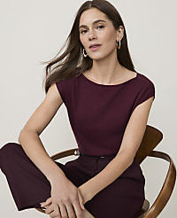 A woman in a maroon top and pants sits on a wooden chair against a plain, light background. carousel Product Image 1
