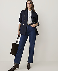A woman in a navy blazer and jeans stands against a plain background, holding a dark tote bag. carousel Product Image 1