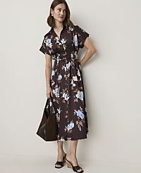 A woman in a floral dress stands against a plain background, holding a dark tote bag. carousel Product Image 1