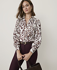 A woman in a patterned blouse and burgundy pants holds a dark brown bag in front of a plain, light-colored background. carousel Product Image 1