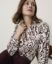 A woman in a patterned blouse and burgundy pants is seated against a plain background. carousel Product Image 3