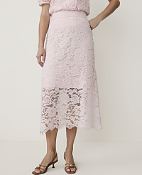 A woman in a light pink lace skirt and matching top stands against a plain white background, her feet adorned with brown heeled sandals. carousel Product Image 2