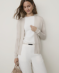 A woman in a cream cardigan and white pants stands against a plain white background, holding a beige handbag. carousel Product Image 1
