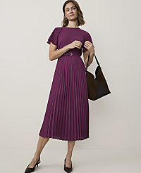 A woman in a plum-colored pleated dress and black heels stands against a plain, light background, holding a dark brown and black tote bag. carousel Product Image 1