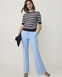 A woman in a striped sweater and light blue flared pants stands against a plain, light background, holding a dark clutch. carousel Product Image 4