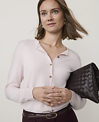A woman in a light pink cardigan and dark trousers holds a woven clutch in front of a plain background. carousel Product Image 1