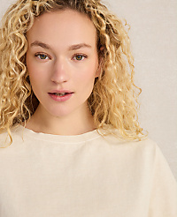 A young woman with curly blonde hair and fair skin looks forward, wearing a cream-colored shirt against a textured, light-colored background. carousel Product Image 2