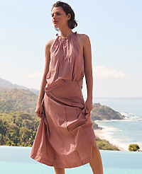 A woman in a pink halter dress stands by a pool with a scenic ocean and mountain view in the background. carousel Product Image 6
