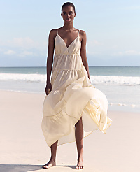 A woman in a flowing cream dress stands on a sandy beach with gentle waves and a clear sky in the background. carousel Product Image 6