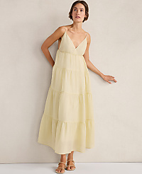 A woman in a flowing yellow tiered dress stands against a plain, textured wall. carousel Product Image 1