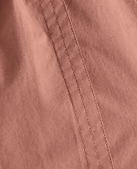 A close-up of a pink fabric with visible stitching runs diagonally across the frame, with soft folds creating subtle shadows in the background. carousel Product Image 3