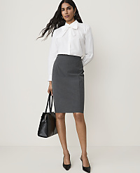 A woman in a white blouse and gray skirt stands against a plain white background, holding a black handbag. carousel Product Image 1