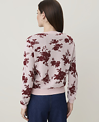A woman in a pink floral sweater and blue jeans stands against a plain, light background. carousel Product Image 2