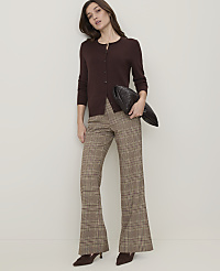 A woman in a brown cardigan and plaid flared pants stands against a plain, light-colored wall, holding a dark clutch. carousel Product Image 4