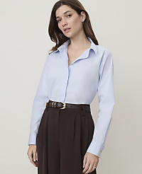 A woman in a light blue collared shirt and dark brown pants stands against a plain, light gray background. carousel Product Image 1