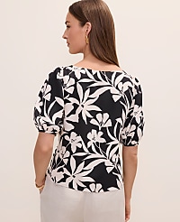 A woman in a black and white floral top and white pants stands against a plain, light background. carousel Product Image 2