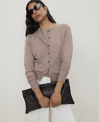 A woman in sunglasses and a beige cardigan holds a dark brown woven clutch in front of a plain white background. carousel Product Image 3