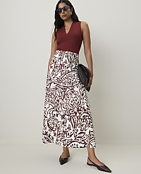 A woman in a maroon top and a patterned skirt stands against a plain background, holding a black clutch. carousel Product Image 1