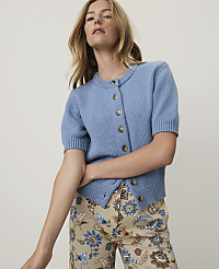 A woman in a blue cardigan and patterned pants stands against a plain, light background. carousel Product Image 1