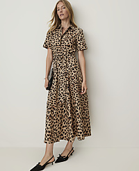 A woman in a leopard-print dress and black kitten heels stands against a plain, light-colored wall, holding a black clutch. carousel Product Image 1