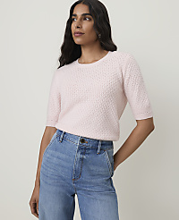 A woman in a pink sweater and blue jeans stands against a plain background. carousel Product Image 1