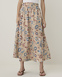 A person stands wearing a beige floral skirt with blue and rust-colored patterns, against a plain, light background. carousel Product Image 2